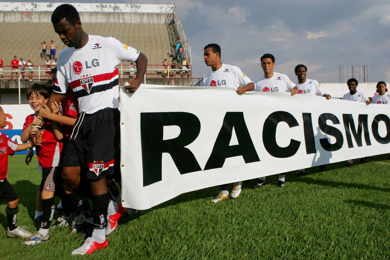 Jogadores entram em campo com uma faixa escrita Racismo