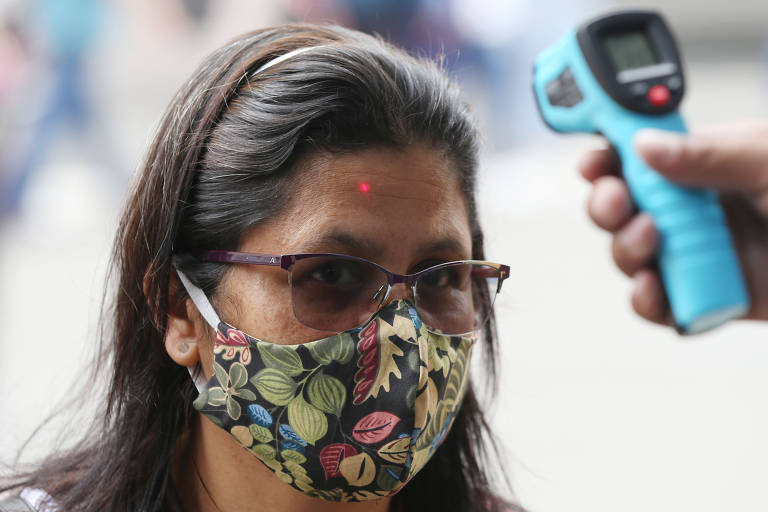 Funcionário de loja mede a temperatura de cliente na entrada do estabelecimento na rua 25 de Março, no centro de SP