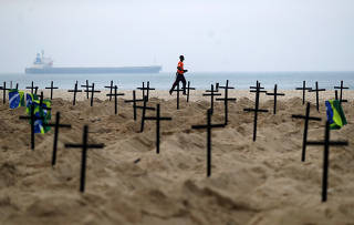 A man runs past the one hundred graves which were dug by activists of the NGO Rio de Paz on Copacabana beach symbolising the dead from the coronavirus disease (COVID-19), in Rio de Janeiro