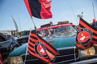 Fans watch local soccer match from their cars outside stadium in Herning