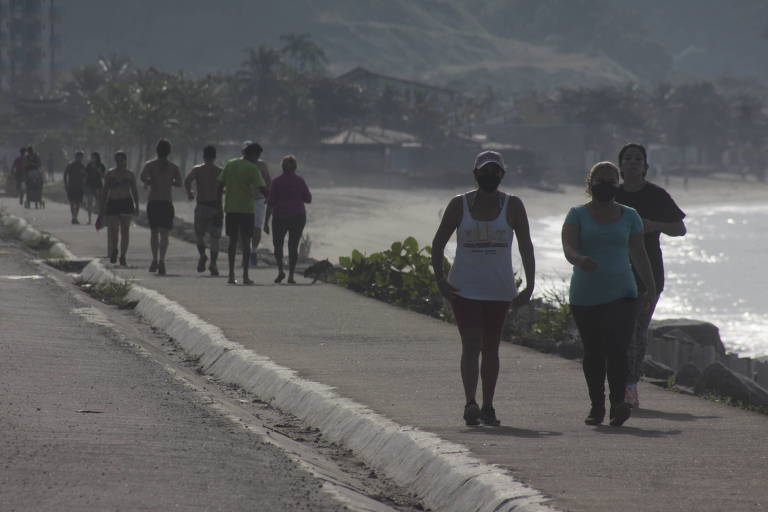 Pessoas caminham em calçada de praia do litoral norte de SP
