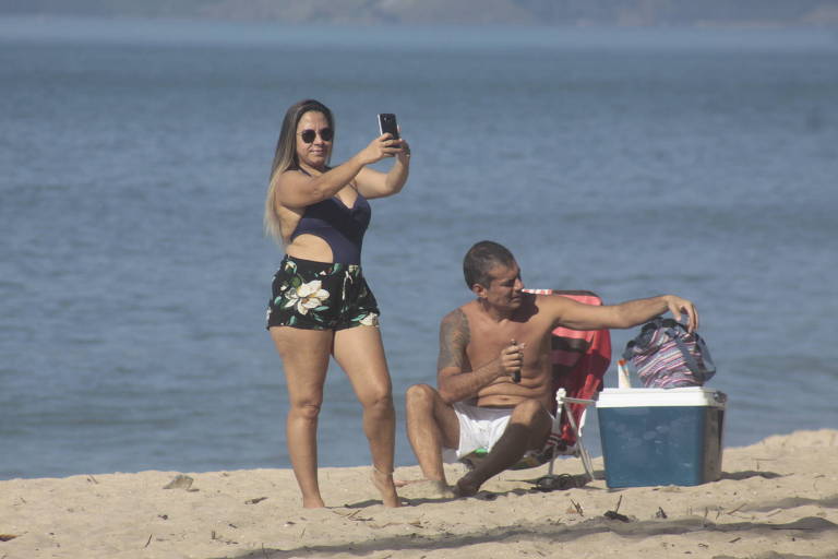 Mulher aproveita dia de sol na praia e tira fotografia em frente ao mar