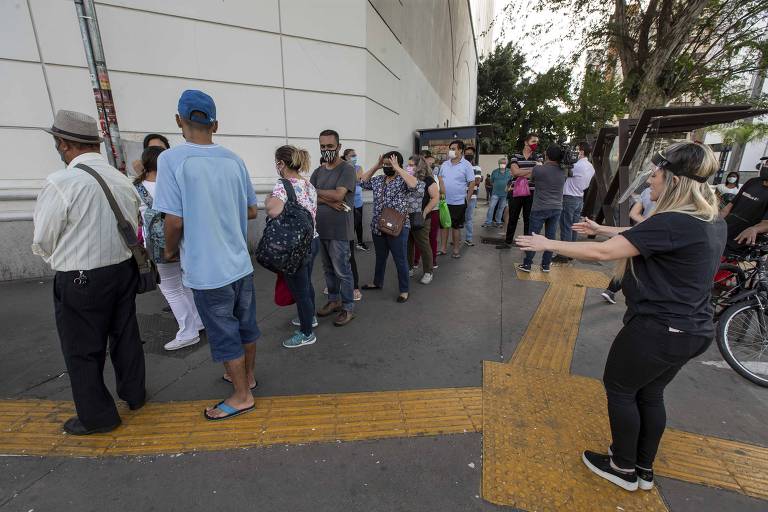 Mulher tenta organizar a fila e manter a distancia de 1,5 metros recomendada pelas autoridades, na reabertura do Shopping Metrô Santa Cruz.