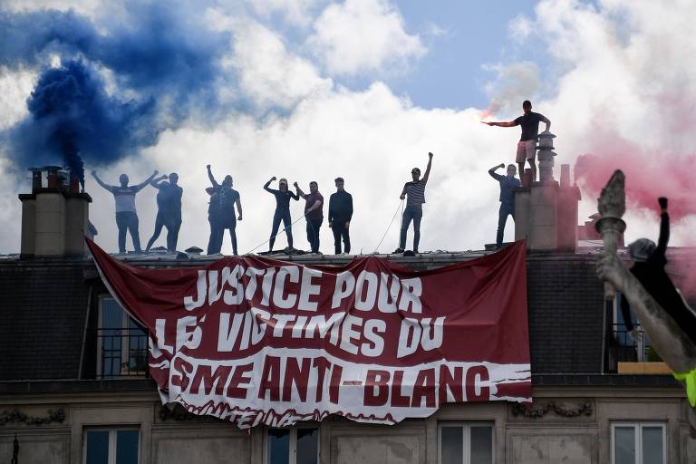 Membros do grupo de extrema direita Generation Identitaire estendem faixa pedindo "justiça para as vítimas do racismo antibranco" em telhado próximo à praça da República durante ato antirracismo em Paris