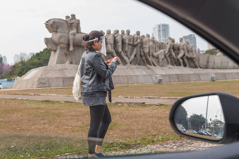 Mulher usando viseira caminha em frente ao Monumento às Bandeiras, perto do Parque Ibirapuera.