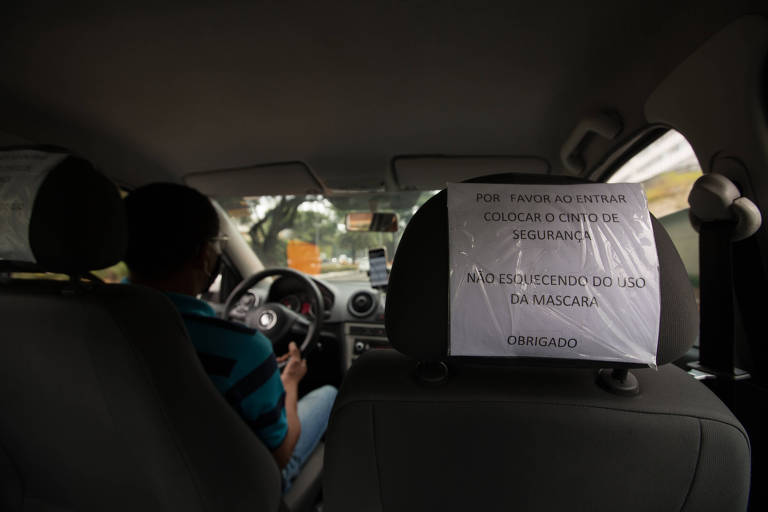 Aviso em carro de applicativo lembra do uso do cinto de segurança e da máscara de proteção.