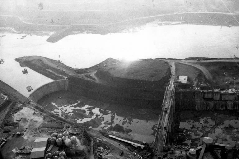 A imagem em preto e branco é a vista aérea da usina hidrelétrica de Itaipu durante a construção em outubro de 1978, localizada no rio Paraná, fronteira entre Brasil e Paraguai, na cidade de Foz do Iguaçu