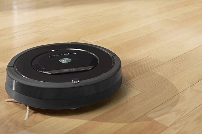 Foto mostra um robô-aspirador Roomba, na cor preta, em cima de um chão de madeira