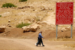 FILE PHOTO: Palestinians walk past a sign with information on Area 
