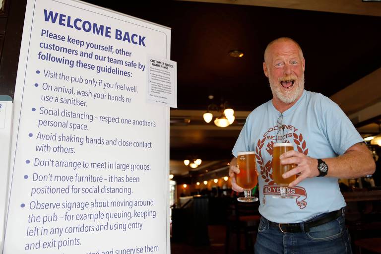 Inglês carregando dois "pints" de cerveja celebra a reabertura do pub Wetherspoon, no leste de Londres, que recepciona seus clientes com a placa "welcome back"