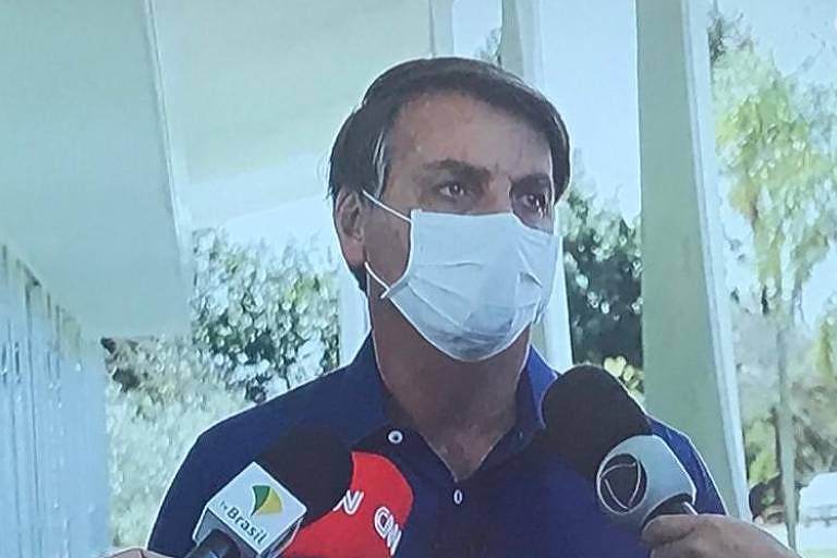 Bolsonaro usando máscara e cercado por microfones