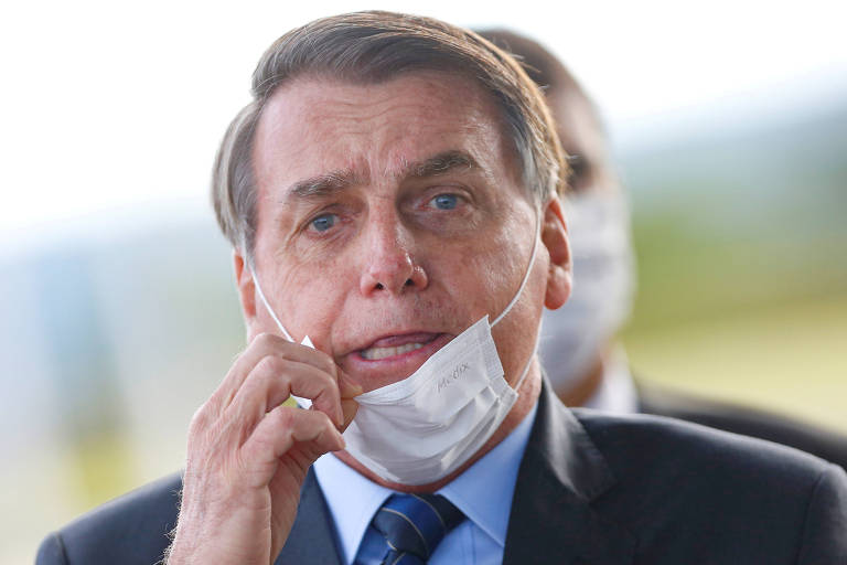 O presidente Jair Bolsonaro tenta ajustar máscara ao deixar o Palácio da Alvorada, em maio