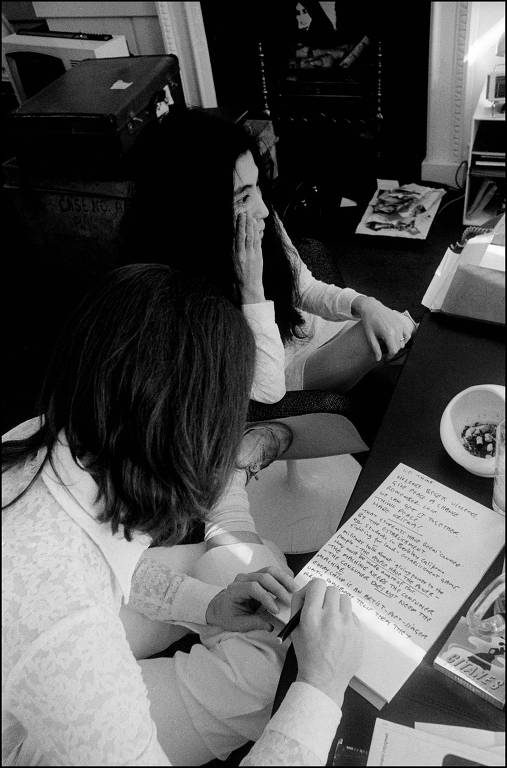John Lennon escreve uma letra de música em uma folha de papel, ele está ao lado de Yoko Ono