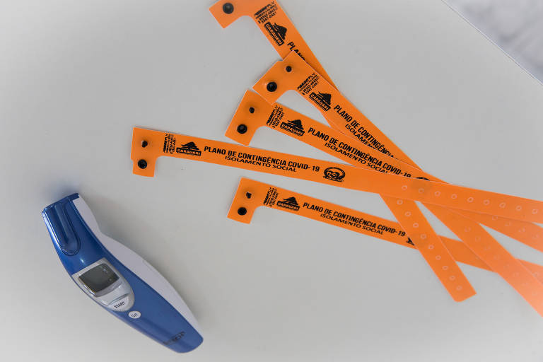 Fitas laranjas que são colocadas no pulso de pessoas que entram na cidade e precisam cumprir quarentena de 14 dias