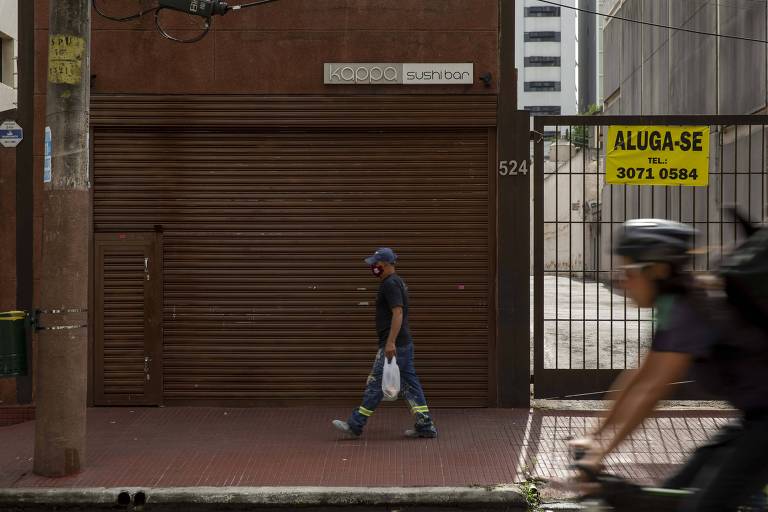Ciclista passa em fretne a portão onde placa amarela anuncia que imóvel está para alugar