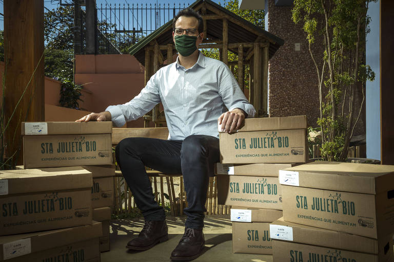 Rafael, vestindo máscara de proteção, está sentado em meio a caixas de papelão