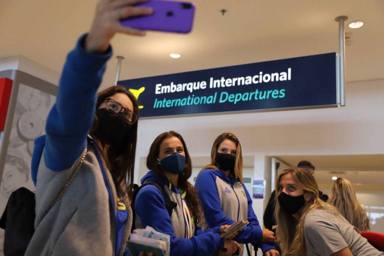 Atletas do nado posam para selfie de máscaras embaixo de placa escrita "embarque internacional", no aeroporto de Viracopos