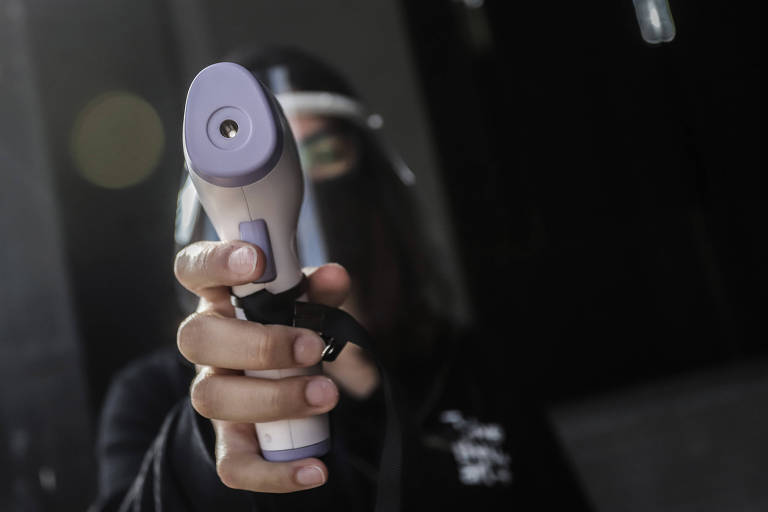 Uma pessoa aponta o termômetro digital, em forma de pistola, para a câmera
