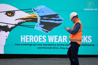 An essential worker wearing a face mask walks past a 'Heroes Wear Masks' sign in Melbourne, the first city in Australia to enforce mask-wearing to curb a resurgence of COVID-19