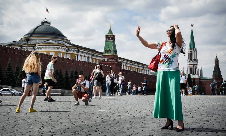 Mulher tira selfie em praça, com construções típicas da Rússia ao fundo 