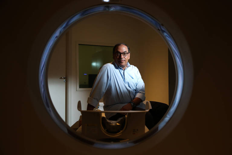 Renato Velloso posa para foto no centro de um enquadramento circular formado por um aparelho de exame