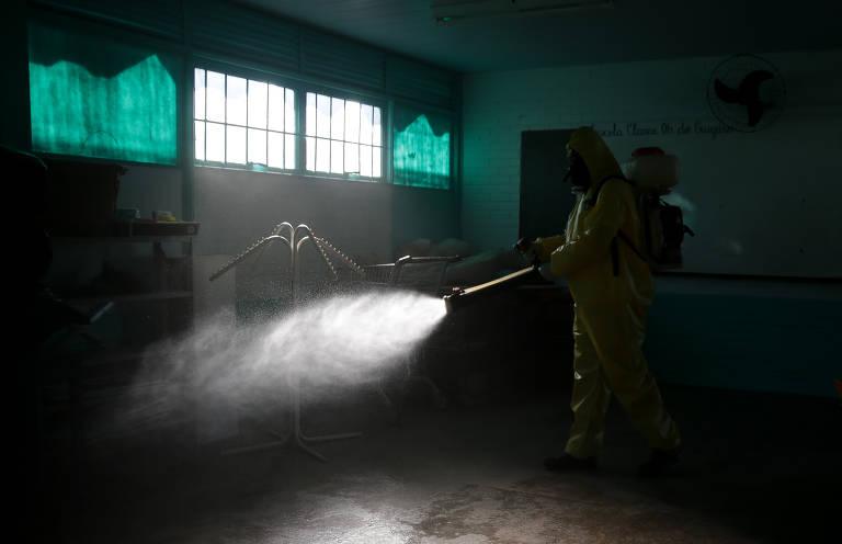 Agente com roupa de proteção e equipamentos aplica produtos químicos para desinfecção no interior de sala de aula