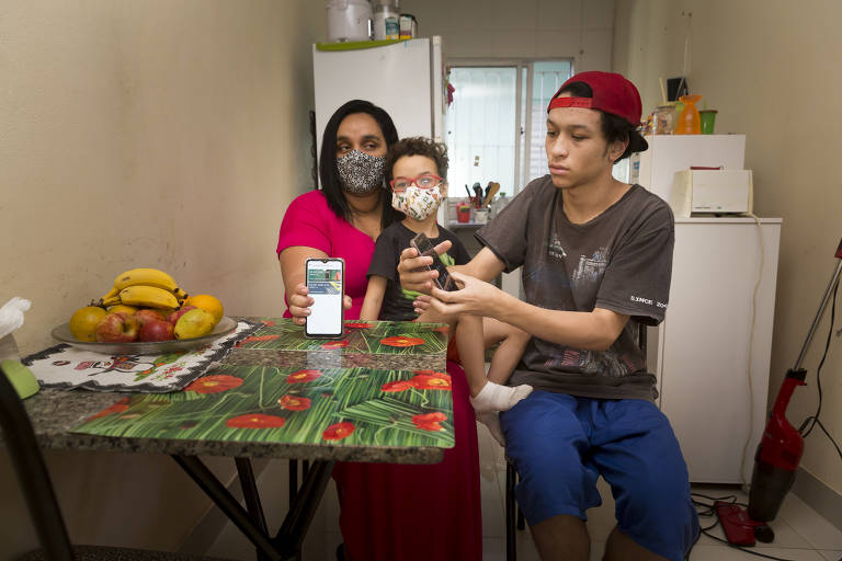 A desempregada Daniele Leite e os filhos Vitor, 5, e Danillo, 16; com sinal fraco de internet e sem computador, eles assistem às aulas de ensino a distância da rede municipal pelo aparelho celular