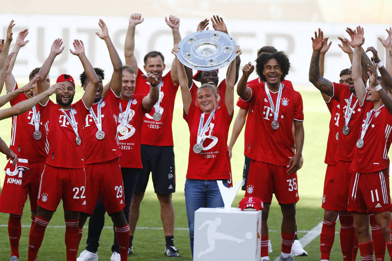 Kathleen Krüger levanta o troféu do título alemão deste ano, observada pelos jogadores da equipe do Bayern de Munique