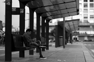 A stranded passenger looks at his phone as he sits at a bus stop during a one-day nationwide strike in Buenos Aires