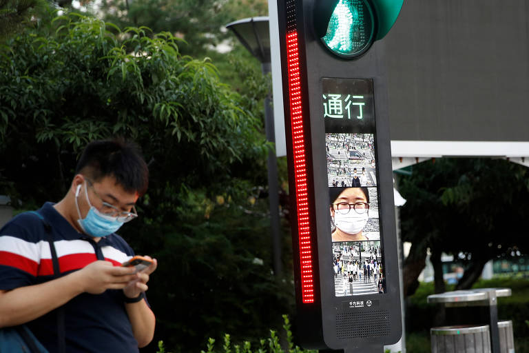 Homem usa celular enquanto aguarda para atravessar rua em Pequim, na China; governo colocou anúncios sobre uso de máscaras em semáforos da capital por causa da pandemia do novo coronavírus
