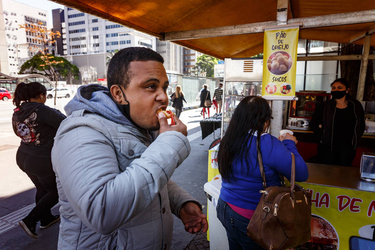 O vendedor Felipe Silva, 26 anos, consome coxinha em uma barraca da avenida Paulista, região central de SP