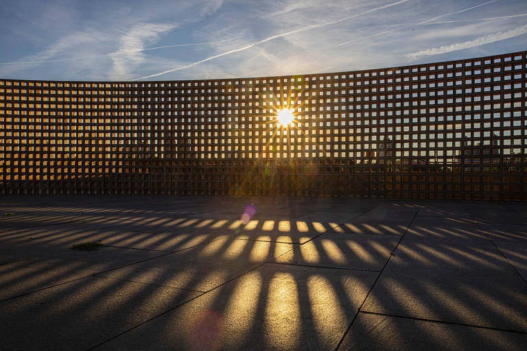 Imagem mostra muro com 33 metros de comprimento e três de altura, feito com tijolos ocos. O sol atravessa a superfície, criando feixes de luz no chão.