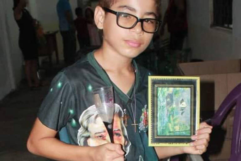 Um menino de óculos segura uma foto e uma taça