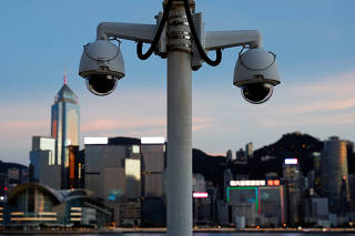 Pair of surveillance cameras are seen along the Tsim Sha Tsui waterfront as skyline buildings stand across Victoria Harbor in Hong Kong