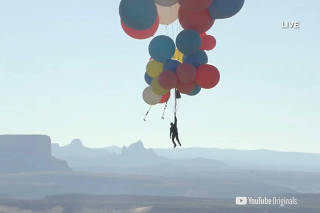 Extreme performer Blaine hangs with a parachute under a cluster of balloons during a stunt to fly thousands of feet into the air over Arizona
