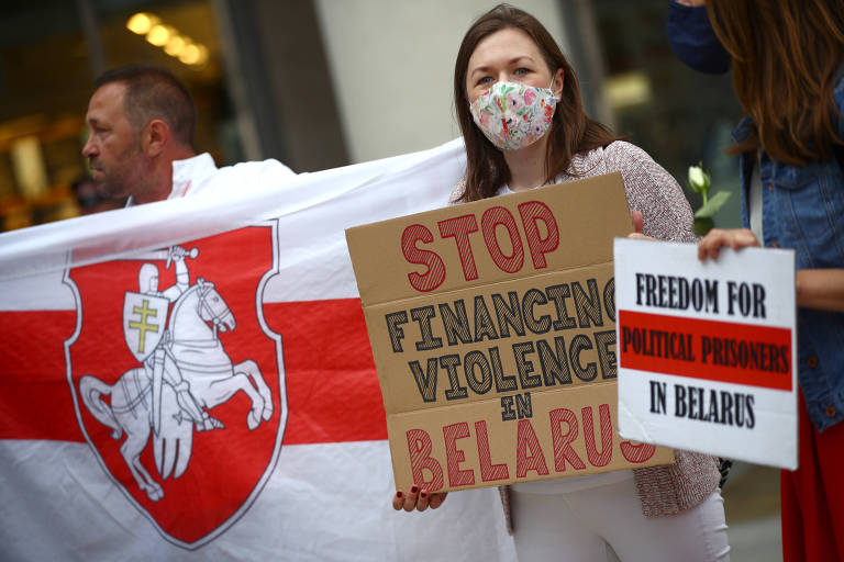 Mulher segura cartaz dizendo parem o finaciamento da violência na Belarus e soltem os prisioneiros políticos