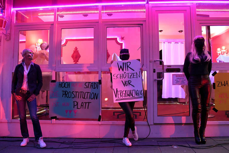 Prostituta em Hamburgo, na Alemanha, seguram cartaz que diz "nós protegemos do estupro" em frente a um bordel com luzes rosa