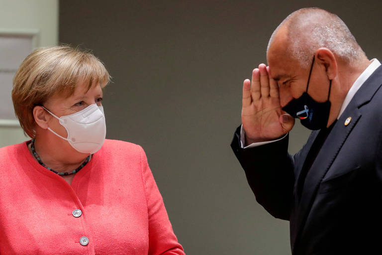 Merkel de jaqueta salmão e máscara branca olha para Borisov, de paletó preto e máscara preta, que bate continência