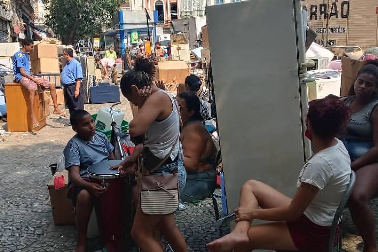 mulheres estão sentadas na calçadas com móveis retirados de um prédio invadido por famílias