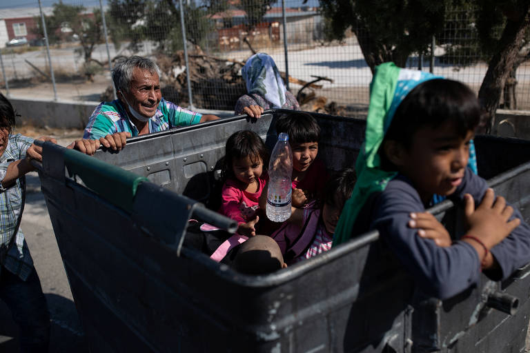 Família usa lixeira para empurrar seus pertences e crianças após ter de abandonar campo de refugiados que pegou fogo na ilha de Lesbos, na Grécia