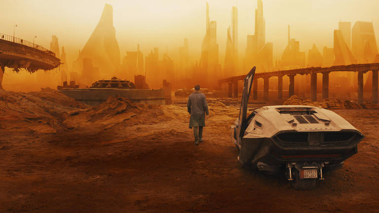 Cena do filme "Blade Runner 2049" mostra homem e veículo futurista em meio a cenário poluído e seco, em tons alaranjados