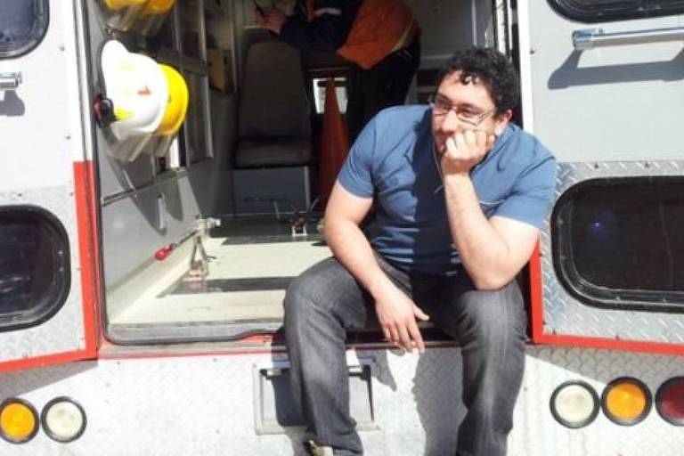 O médico Daniel Gatica está sentado  na porta de uma ambulância