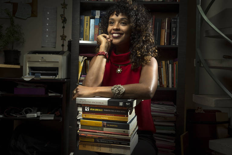 A advogada Haydée Paixão Soula sorri enquanto apoia os braços em uma pilha de livros de Direito