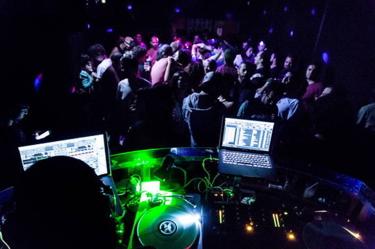 DJ controla música e pessoas dançam na pista