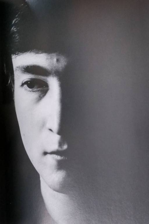 Em preto e branco, rosto de John Lennon, jovem, com a luz incidindo apenas no lado direito de sua face