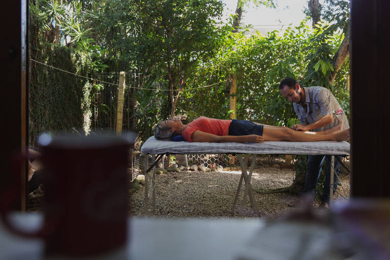 mulher deitada em maca no quintal, cercada de plantas e árvores, faz sessão de acupuntura com médico da família