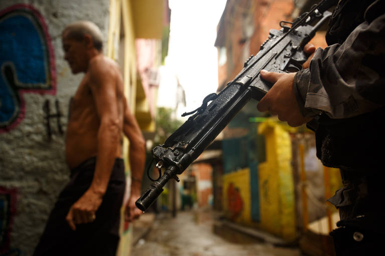 Policiais fazem incursão com ajuda de cão em becos da favela Nova Holanda, no Complexo da Maré, em 2013. Após uma série de ataques coordenados a três favelas com UPPs, a PM iniciou várias ocupações em comunidades da zona norte dominadas pelo Comando Vermelho que não tinham as unidades
