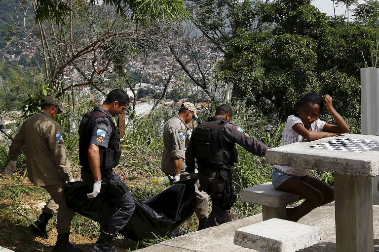 Policiais e bombeiros carregam o corpo de um dos dois homens encontrados mortos no complexo de favelas do São Carlos em 2015. Segundo moradores, havia uma guerra entre traficantes e os dois homens foram mortos pela polícia durante uma operação 