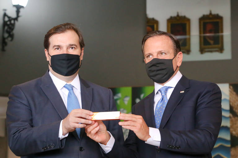 O governador de São Paulo, João Doria (PSDB, ao lado do presidente da Câmara dos Deputados, Rodrigo Maia; ambos seguram juntos uma embalagem da Coronavac