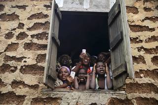 People gather at a window to watch a procession by followers of the Yoruba religion as part of a festival to celebrate the Osun river goddess in Osogbo